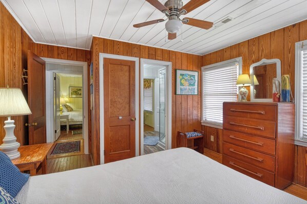 A bedroom with a bed, dresser, ceiling fan, and wooden walls.