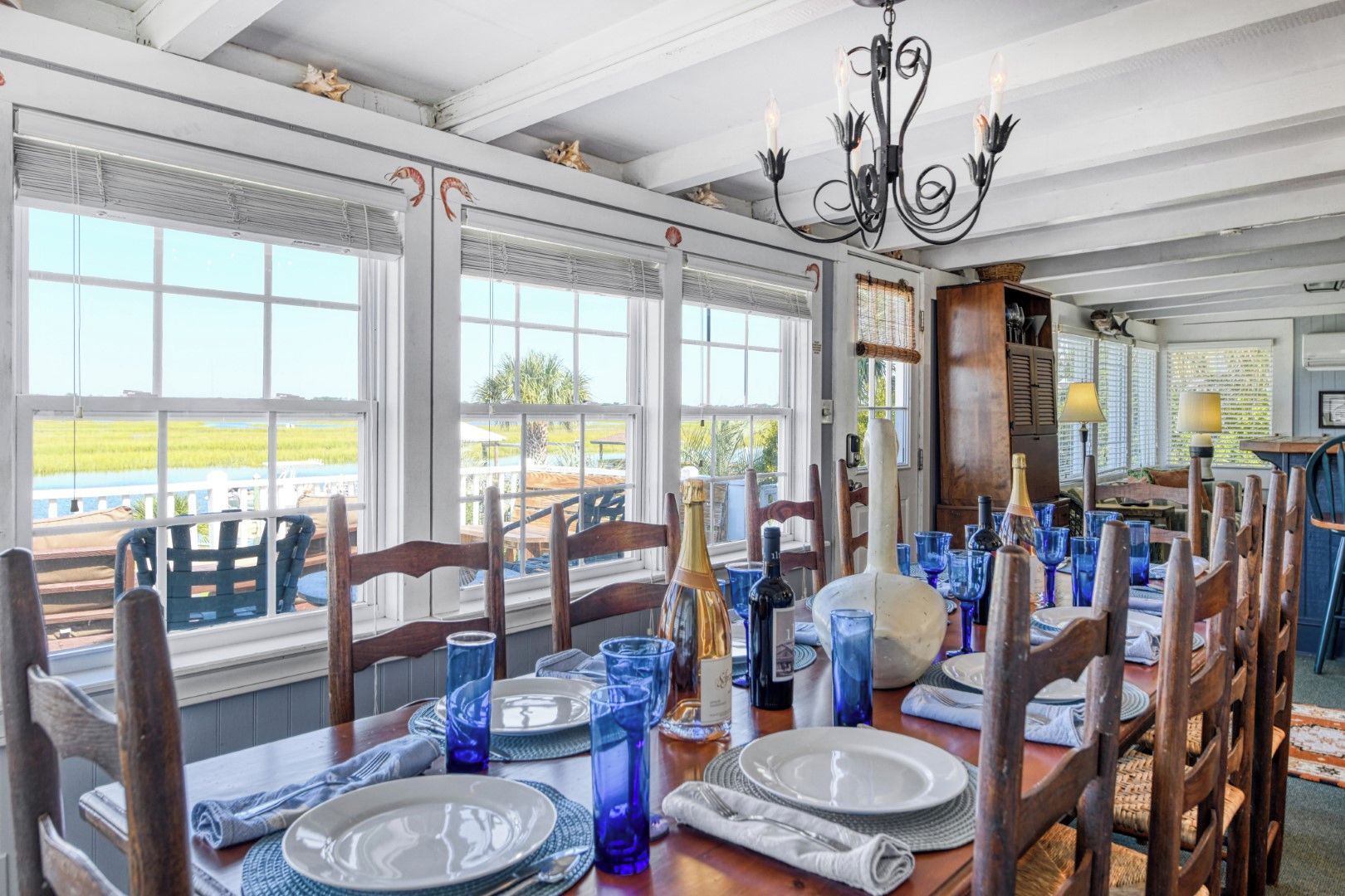 A dining area with a view of the outdoors, featuring a table set with plates, glasses, and a bottle.