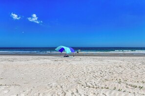 Uma praia com um único guarda-sol e uma pessoa sentada debaixo.