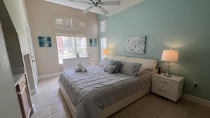 A bedroom with a bed, nightstands, a ceiling fan, and artwork on the walls.