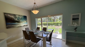 A dining area with a table set for four, chairs, a ceiling light fixture, and a painting on the wall.