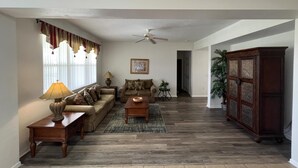 A living room with a sofa set, a coffee table, a lamp, a ceiling fan, and a cabinet. - 5/4 Pool Home With THREE Master Suites In Coveted Windwood Bay Community (Davenport)