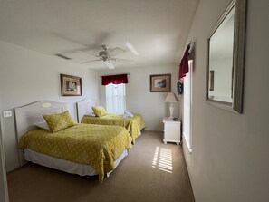 Une chambre avec deux lits, un ventilateur de plafond, une table de chevet avec une lampe et un miroir au mur.