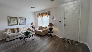 A living room with two sofas, a coffee table, a lamp, and a door. - 5/4 Pool Home With THREE Master Suites In Coveted Windwood Bay Community (Davenport)