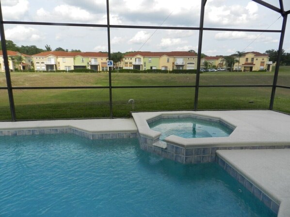Une piscine avec un jacuzzi et une vue sur les immeubles résidentiels, le tout visible à travers une zone protégée par un moustiquaire.