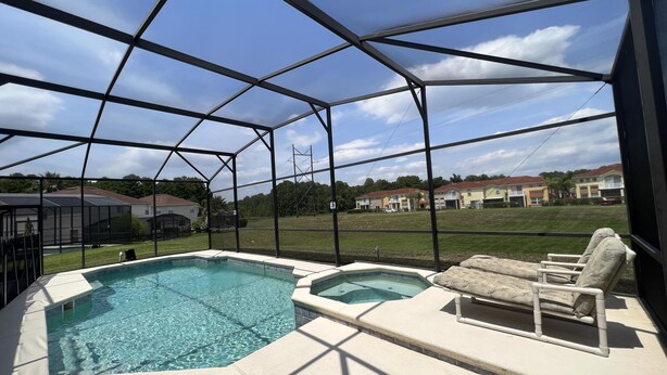 A covered outdoor swimming pool with lounge chairs, a hot tub, and a view of residential buildings. - 5/4 Pool Home With THREE Master Suites In Coveted Windwood Bay Community (Davenport)