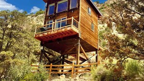 A wooden cabin with a balcony, situated on stilts amidst a rocky landscape with trees. - Stargazing Treetop near Zion with King Bed (Orderville)