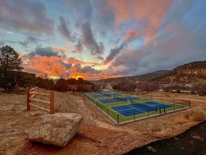 A tennis court with a wooden fence and a large rock nearby. - Stargazing Treetop near Zion with King Bed (Orderville)