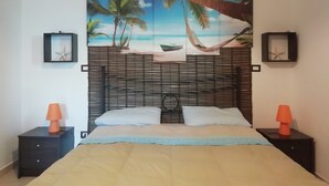 Un dormitorio con cama, dos mesitas de noche, cabecera con un mural con motivos marinos y dos decoraciones de estrellas de mar enmarcadas.