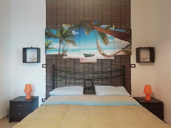 A bedroom with a bed, two nightstands, a headboard with a beach-themed mural, and two framed starfish decorations.