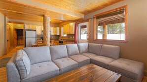 Un salon chaleureux avec un canapé d’angle, un parquet et une grande fenêtre.