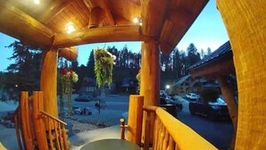 Une terrasse en bois, agrémentée d’une table et de chaises, entourée de rampes de protection, d’où l’on aperçoit un parking et un bâtiment en arrière-plan.