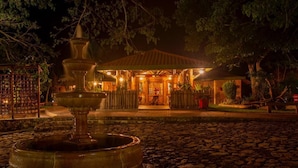 A nighttime scene of a building with a fountain in the foreground, surrounded by trees and a cobblestone path. - Samadhi Ecohotel by Rotamundos (Puerto Escondido)