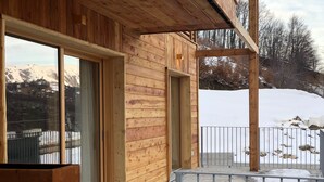A wooden cabin with large windows, a balcony, and a view of snow-covered mountains. - 3 bedroom apartment Chalet Bizet (Panice Soprana)