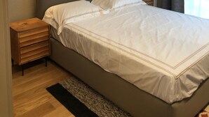 A neatly made bed with white linens, a wooden nightstand, and two wall-mounted light fixtures. - 3 bedroom apartment Chalet Bizet (Panice Soprana)