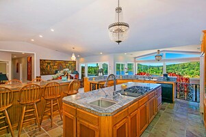 A spacious kitchen with a large island, wooden bar stools, and a view of the outdoors.