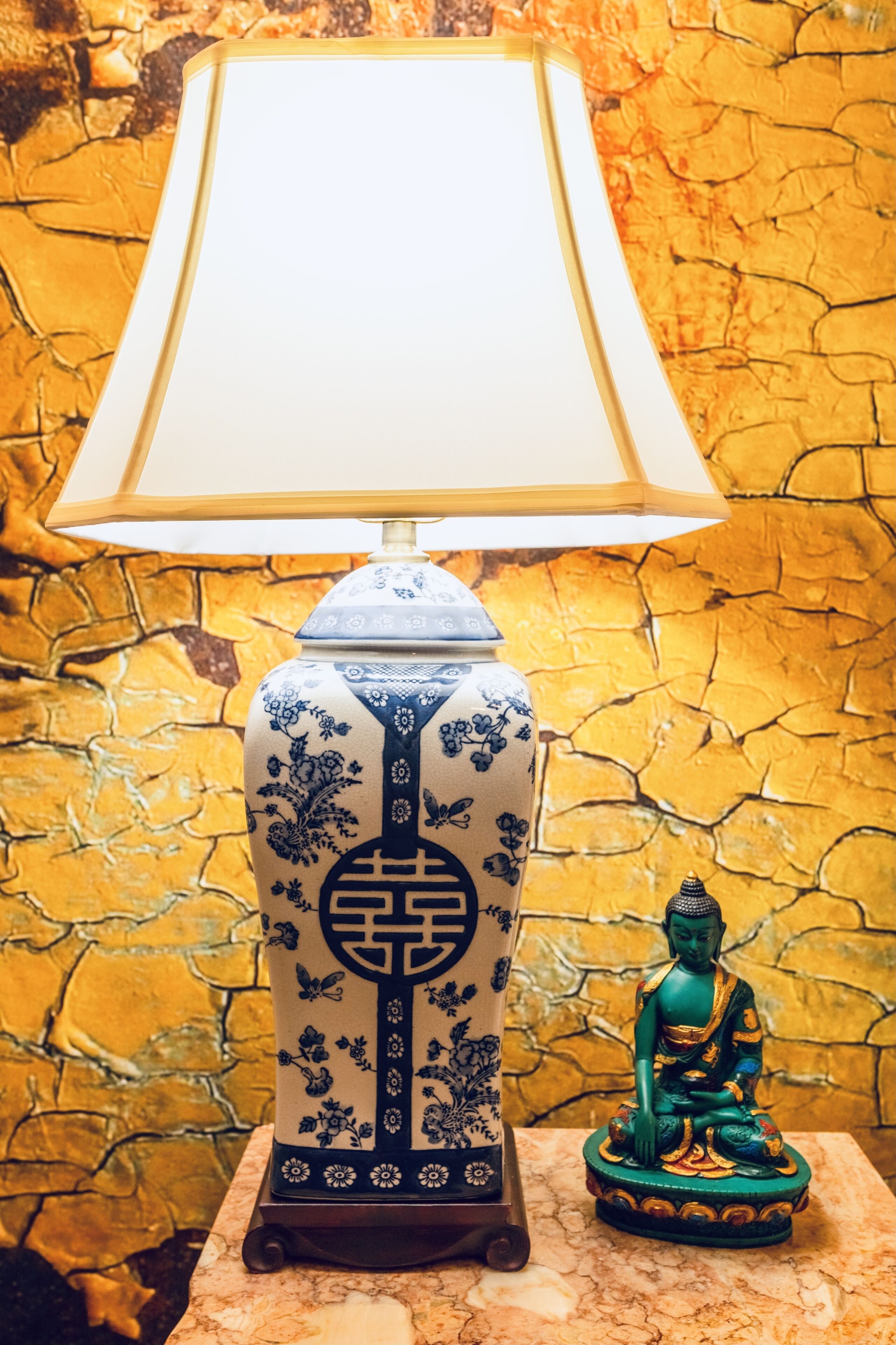 Une lampe aux motifs bleus et blancs, une statue de Bouddha et un mur à la texture particulière.