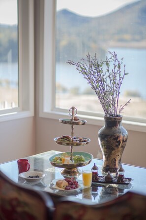 Ein Tisch mit einer Etagerre, auf der Gebäck, eine Obstschale und eine Vase mit Blumen stehen.