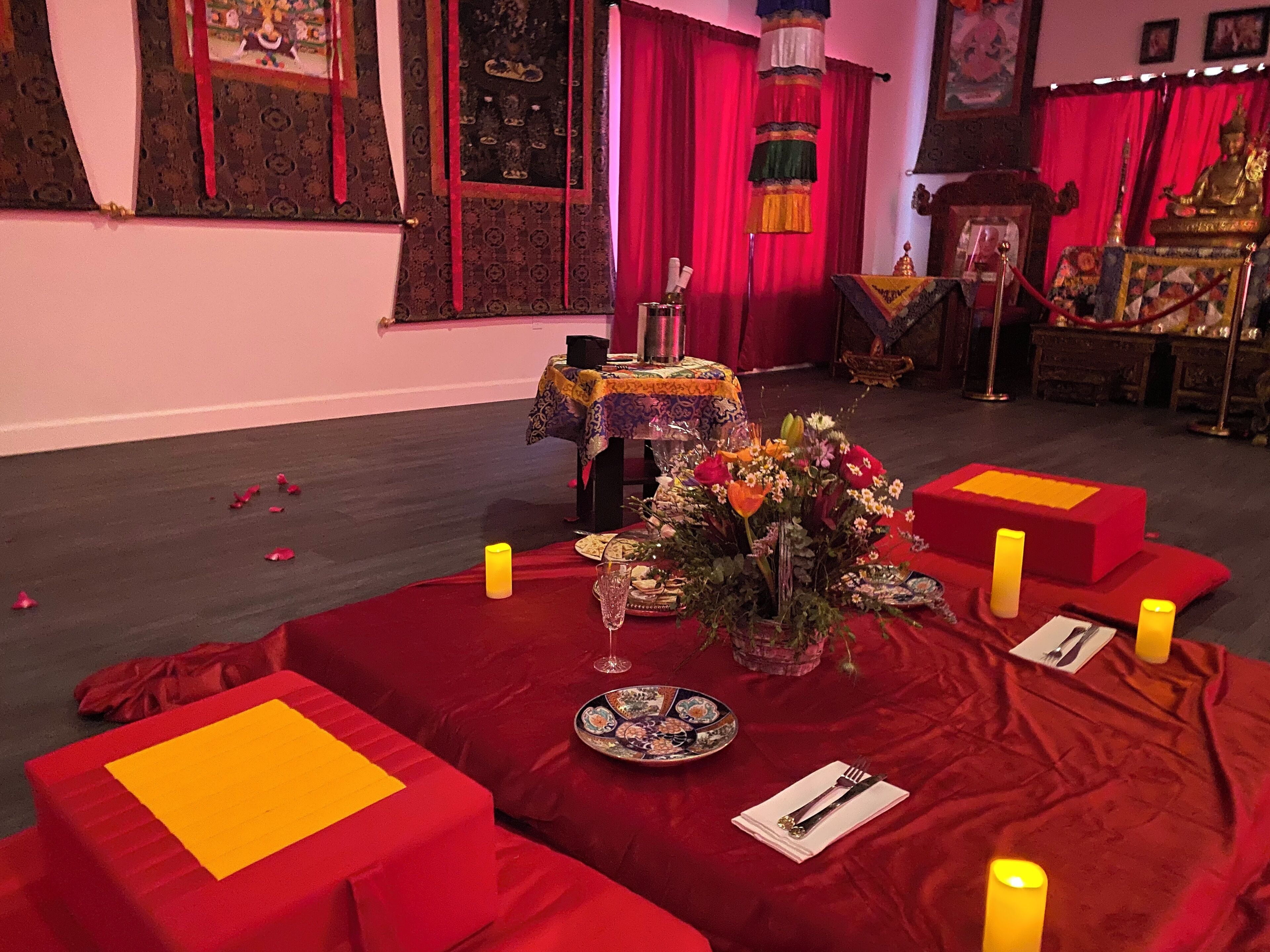 Um quarto com carpete vermelho, uma mesa com um arranjo floral e velas.