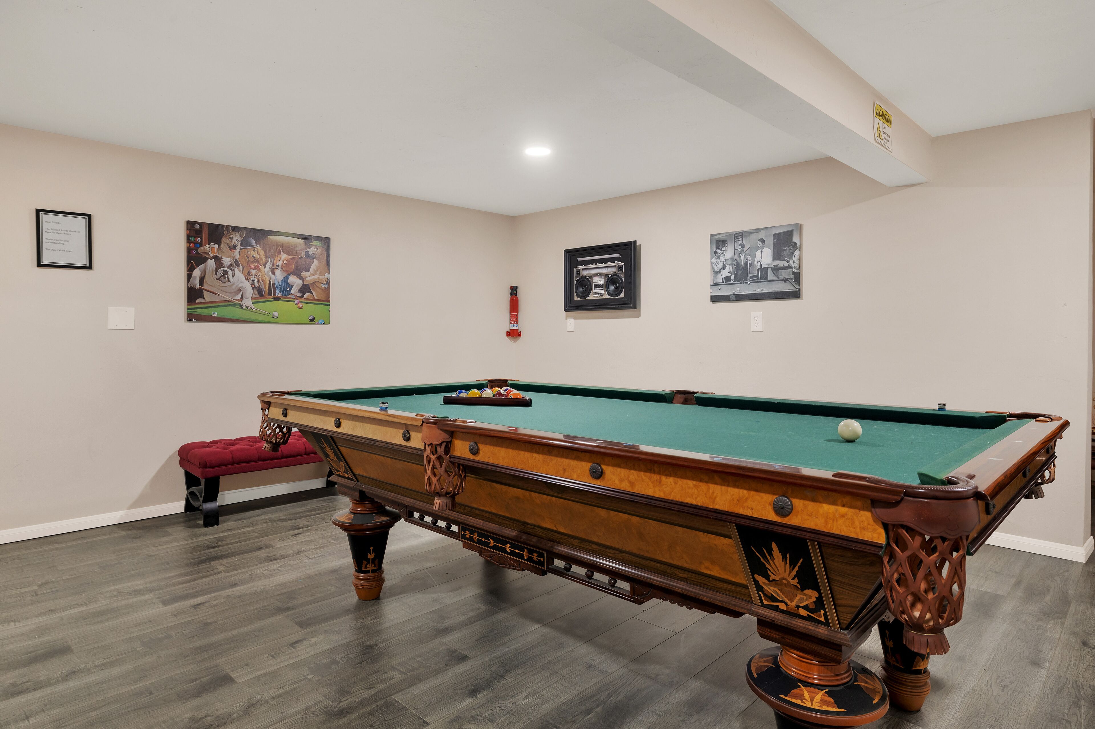 A pool table with a red bench, framed pictures on the walls, and a fire extinguisher.