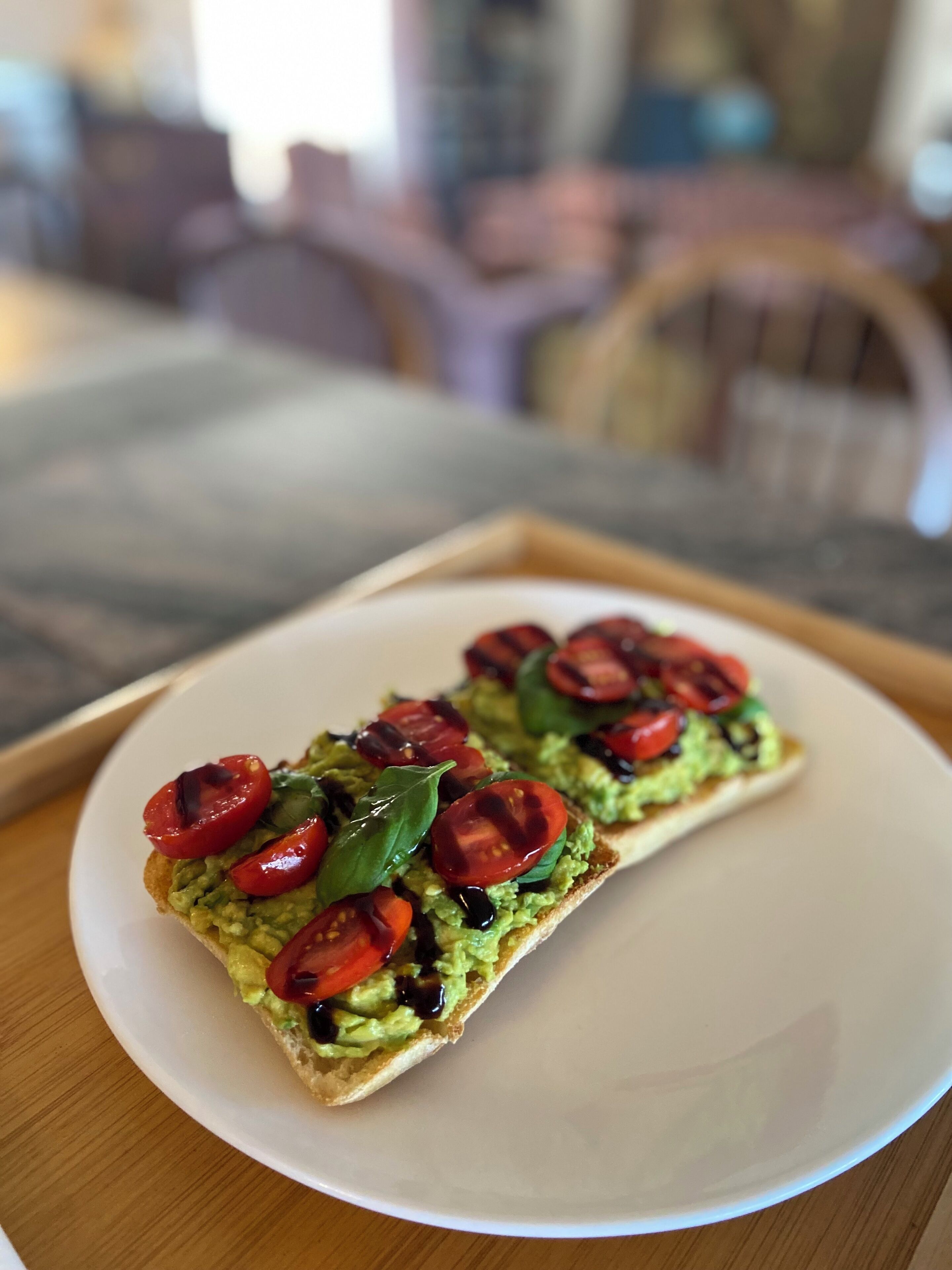 En tallerken med ristet brød, avocado, tomater og basilikum.