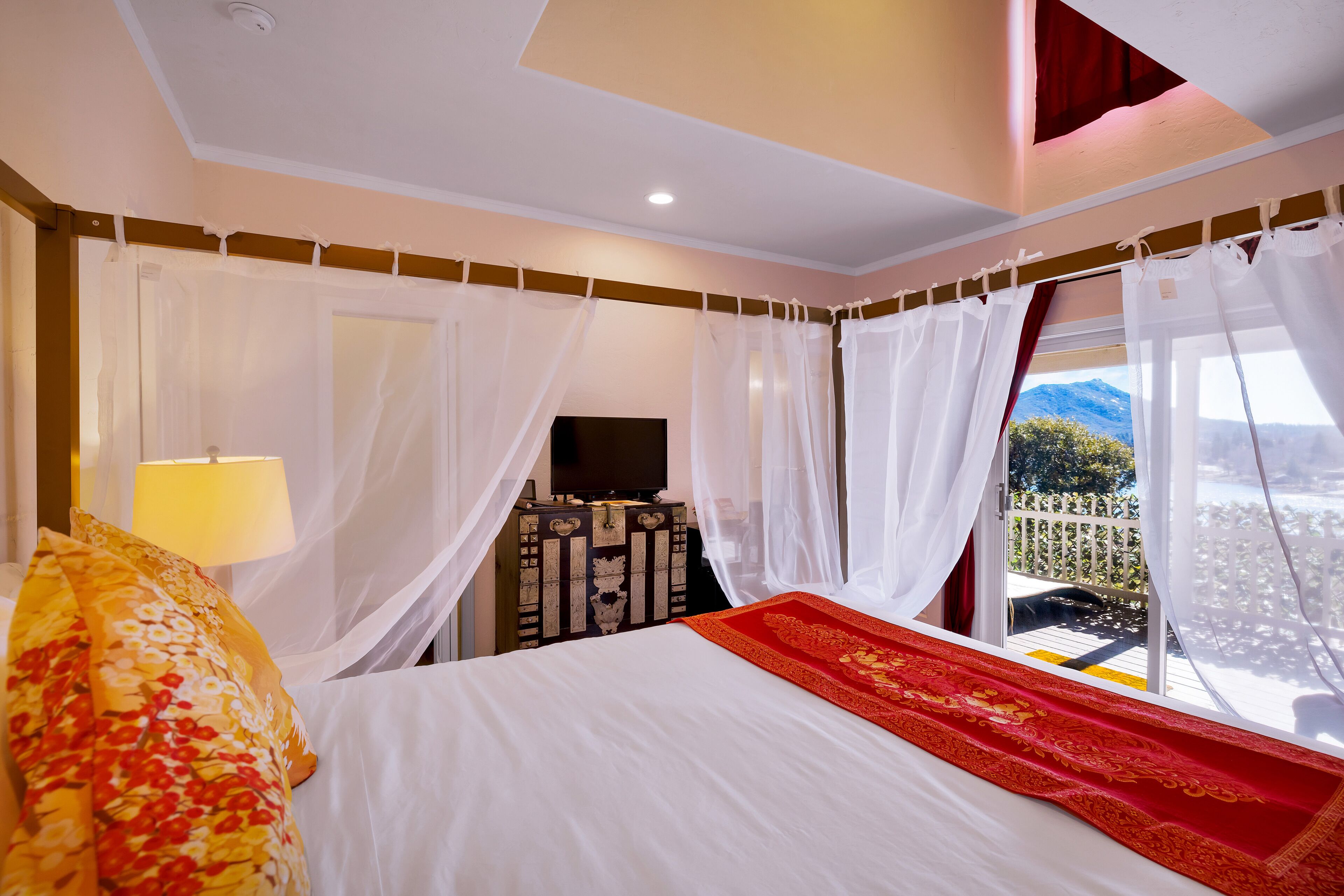 Ein Hotelzimmer mit Bett, Fernseher, Nachttisch und Blick ins Freie.