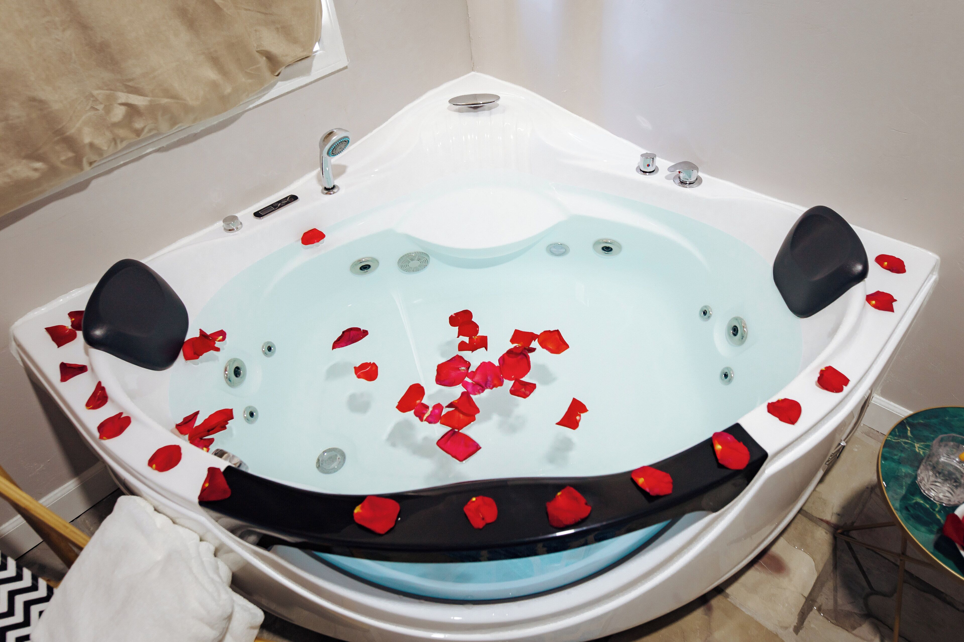 Une baignoire remplie de pétales de rose, une serviette et un verre posés sur une table.