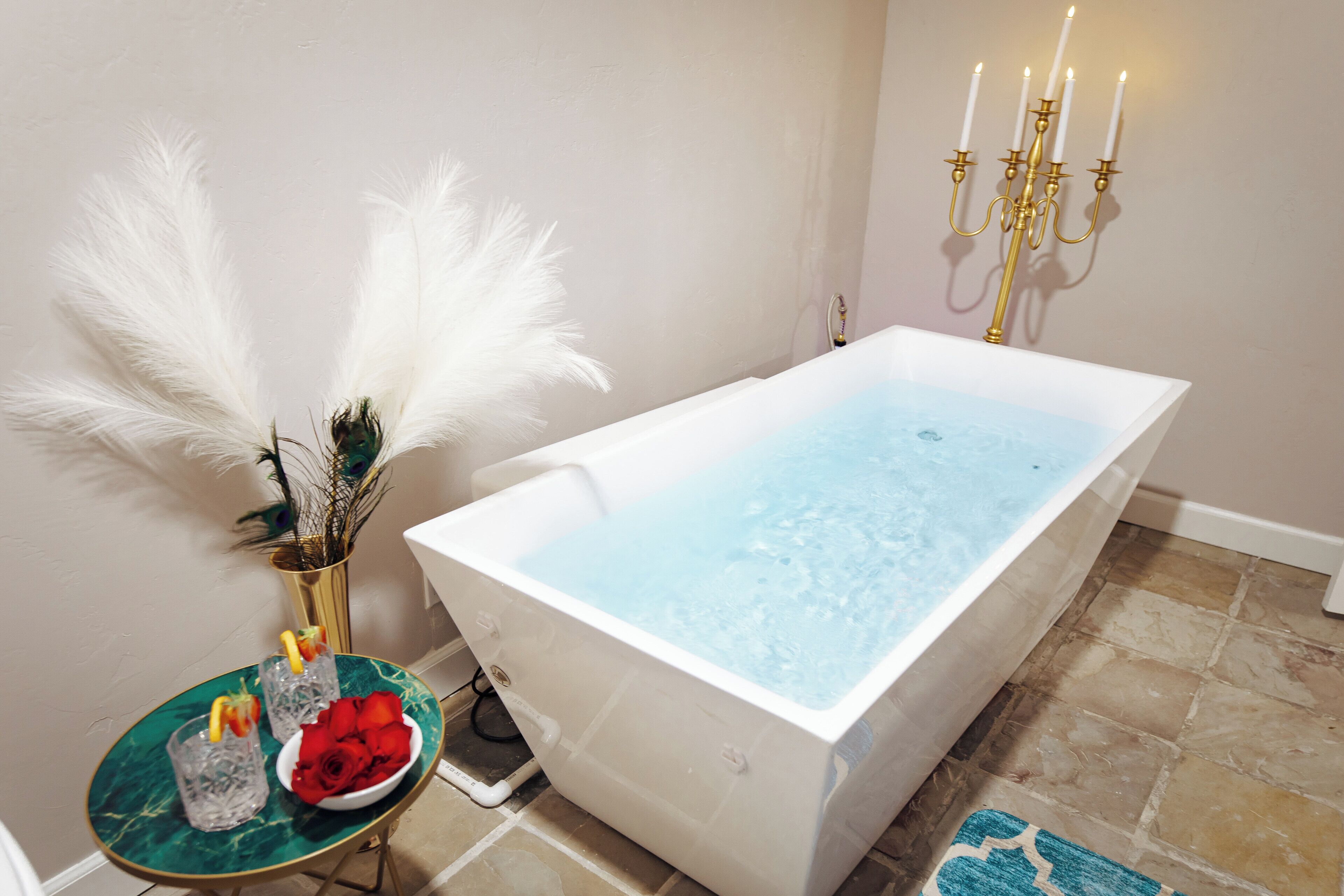 A modern bathroom with a freestanding bathtub, a small table with decorative items, and a candelabra on the wall.