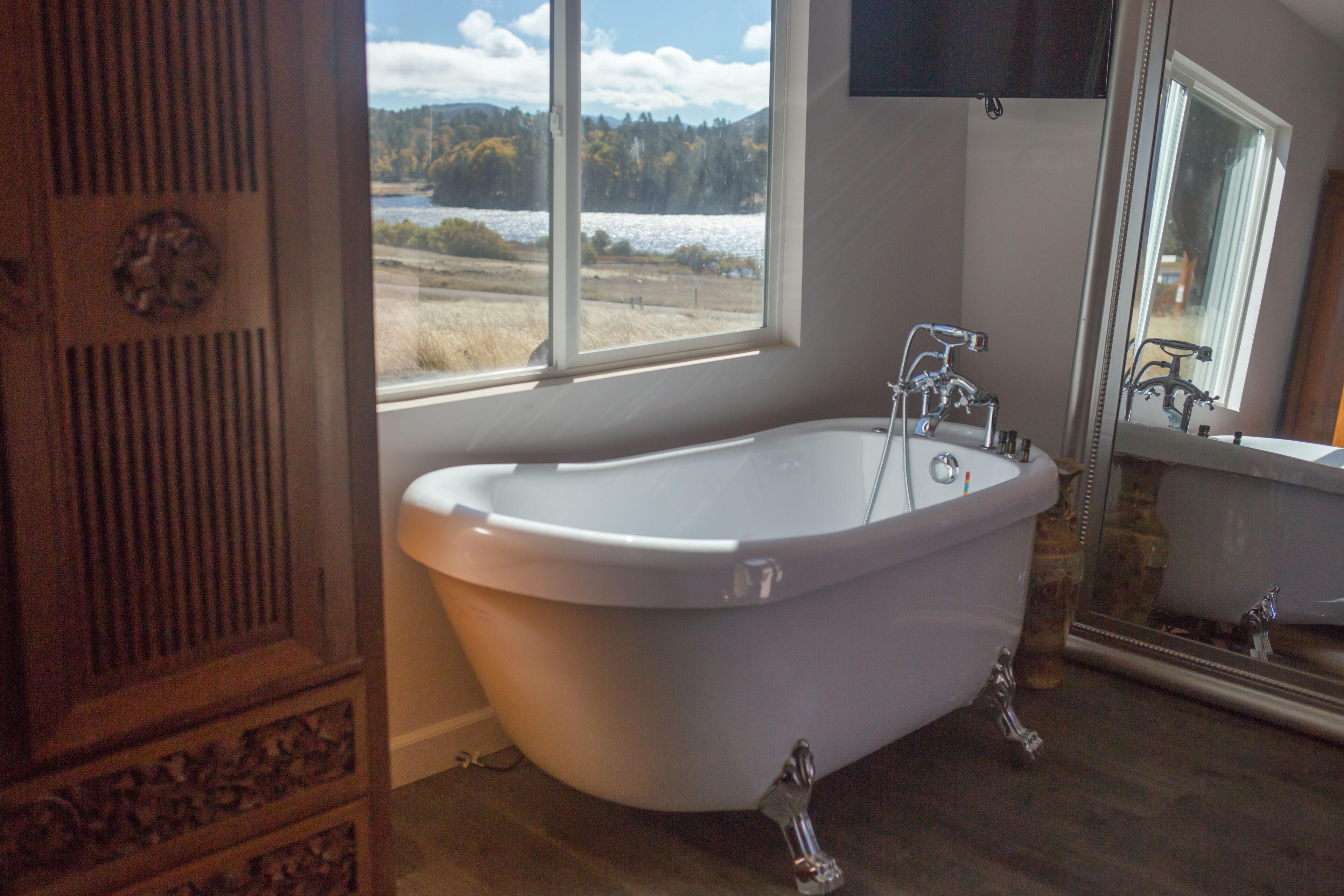 A bathroom with a freestanding bathtub, a window with a view of a snowy landscape, and a wooden cabinet with intricate carvings.