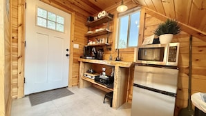 A compact kitchen with wooden walls, a white door, a sink, a microwave, and a refrigerator.