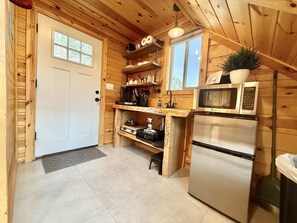 Eine kleine Küche mit Holzwänden, einer weißen Tür, einem Spülbecken, einer Mikrowelle und einem Kühlschrank.