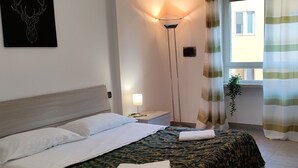 Una habitación de hotel con una cama, una mesita de noche, una lámpara, una ventana con cortinas y una obra de arte en la pared.