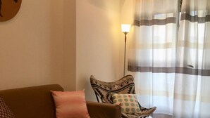 Una sala de estar con un sofá marrón, cojines estampados, una pequeña silla plegable y una lámpara de pie.