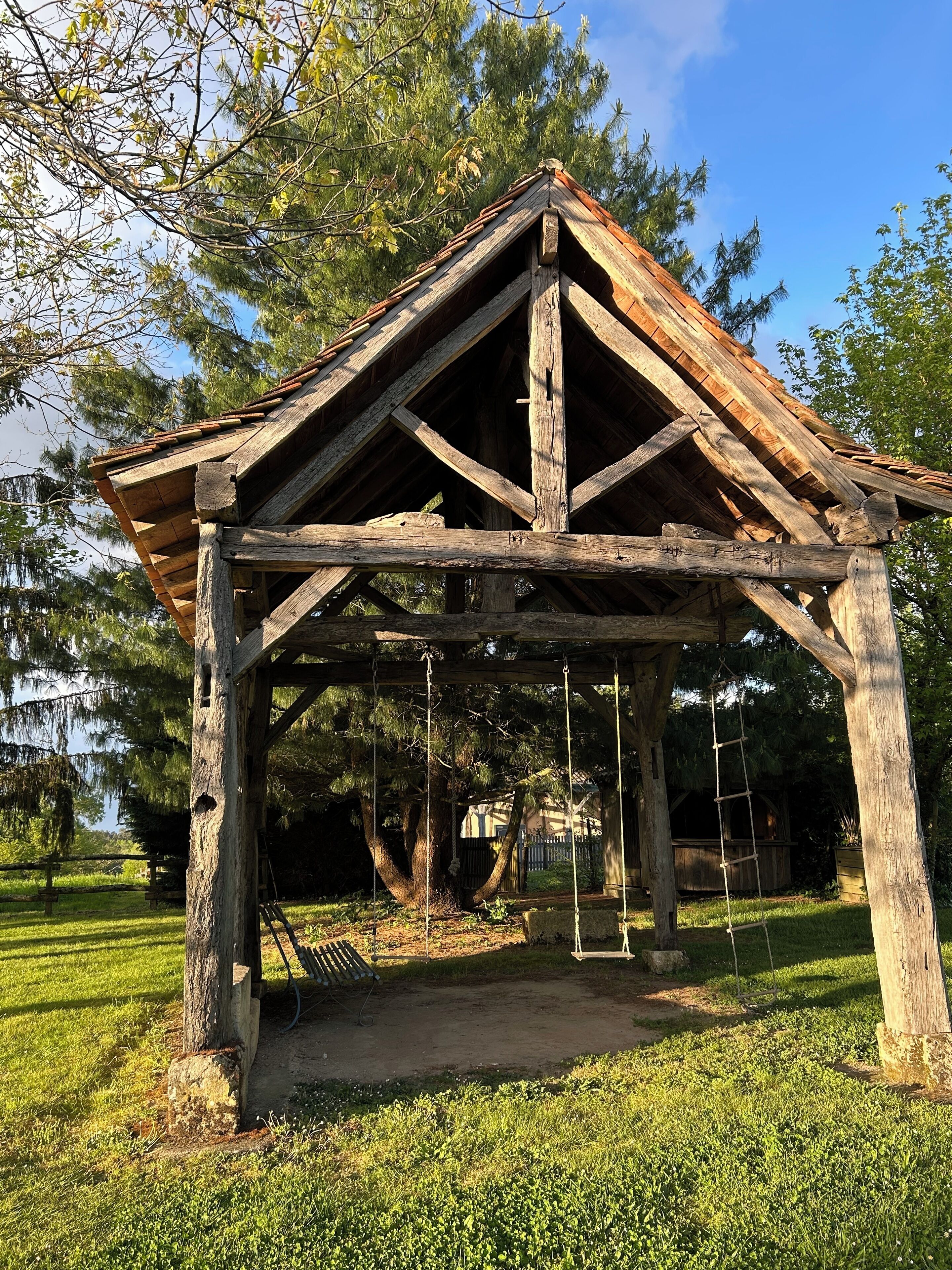 Un quiosco de madera rústico con techo triangular y un columpio.