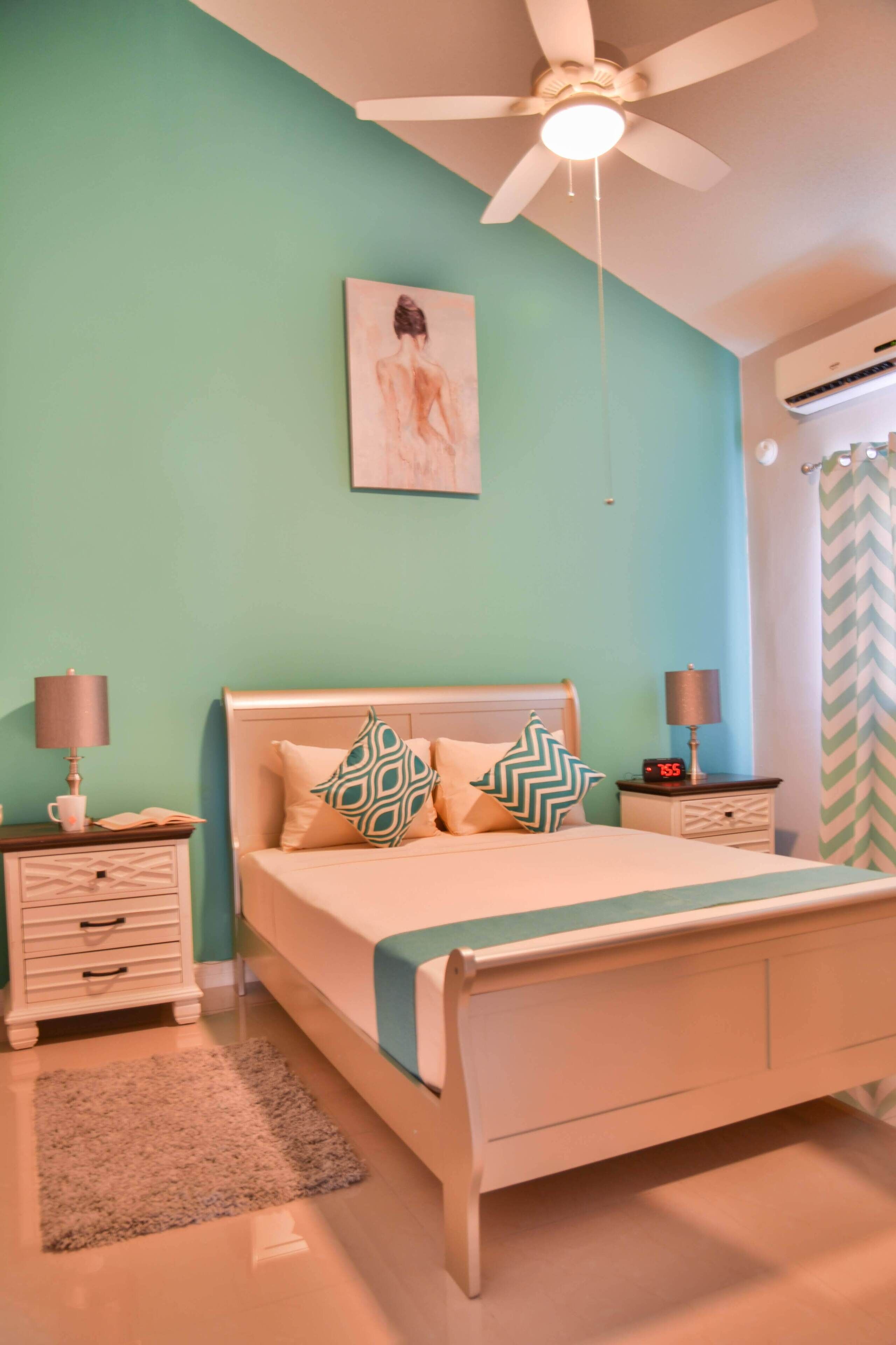 A bedroom with a bed, nightstands, a ceiling fan, and a wall-mounted air conditioner.
