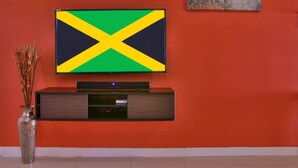 Een flatscreen-tv bevestigd aan een muur, met een Jamaicaanse vlag, een modern tv-meubel eronder en een abstract kunstwerk aan de rechterkant.