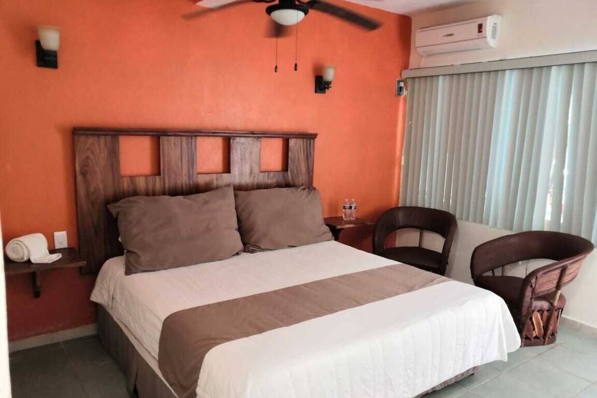 A hotel room with a bed, a chair, a ceiling fan, and a window with blinds.