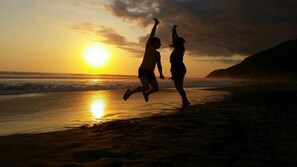 Two people jumping on a beach at sunset.