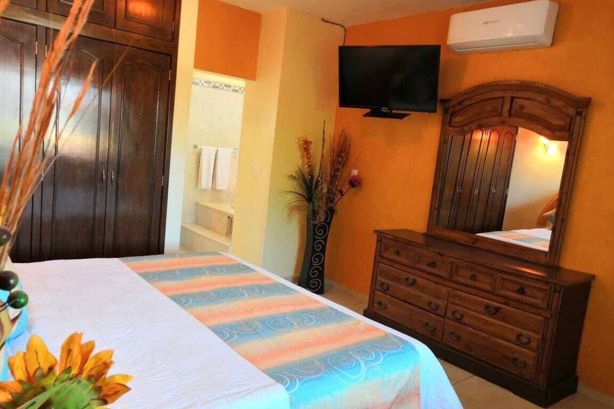 A bedroom with a bed, a dresser, a TV, and a mirror.