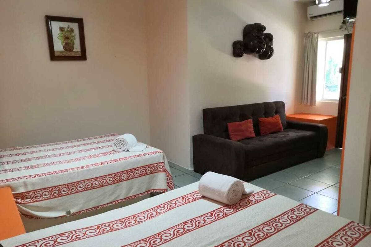 A hotel room with two beds, a sofa, a decorative wall piece, and a window with curtains.