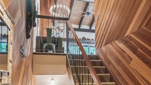 Un escalier en bois, un lustre, un tableau encadré au mur et un ventilateur de plafond.