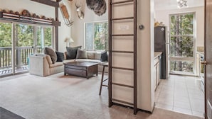 Un vaste espace de vie doté d’un plafond en bois, d’un ensemble de canapés, d’une table basse et d’une échelle.