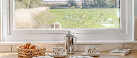 Una mesa de desayuno con una cesta de pan, una cafetera, tazas y un periódico.