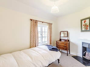 Quarto com cama, cômoda, espelho, lareira e janela com cortinas.
