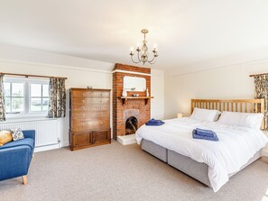 A bedroom with a brick fireplace, a wooden dresser, a bed with white linens, and a blue armchair.