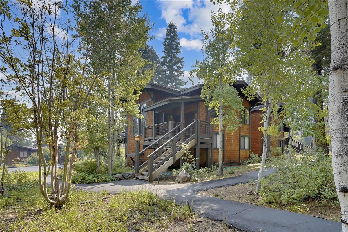 A modern building with a staircase leading to a balcony, surrounded by trees and a paved walkway.