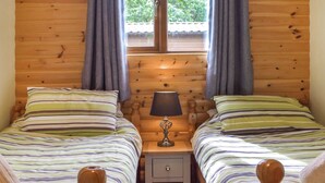 Habitación doble con dos camas, una mesita de noche, una lámpara y un ventanal con cortinas.