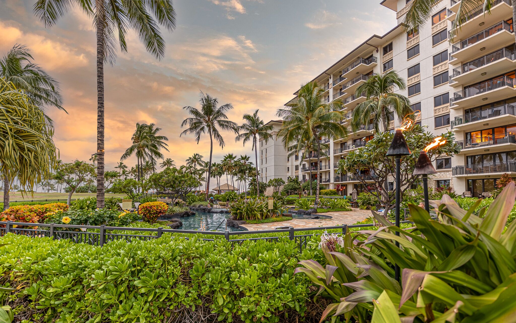 A resort with a pool, palm trees, and a multi-story building with balconies.