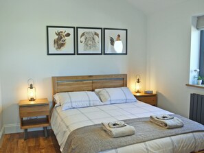 A neatly made bed with a plaid bedspread, two pillows, and two folded towels on the bed. There are two bedside tables with lamps, and three framed animal pictures on the wall above the bed.