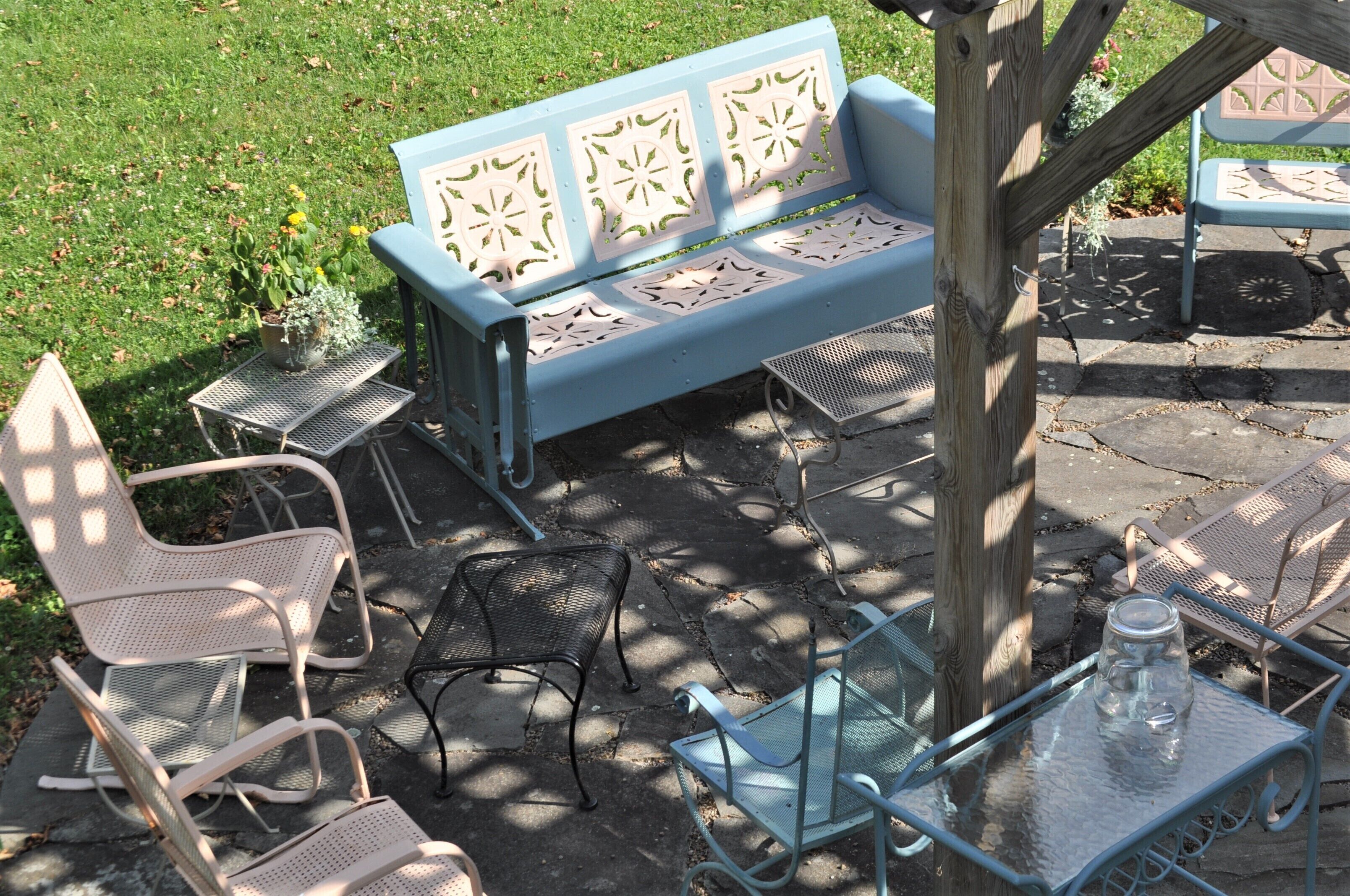A patio with a blue bench, metal chairs, and a glass table with a jar.